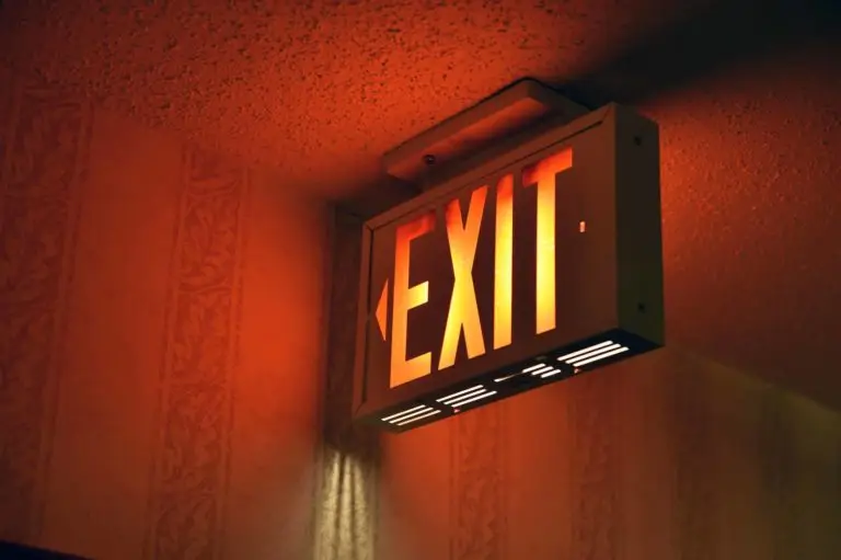 A glowing exit sign casting an orange hue on the wall in a dimly lit area.