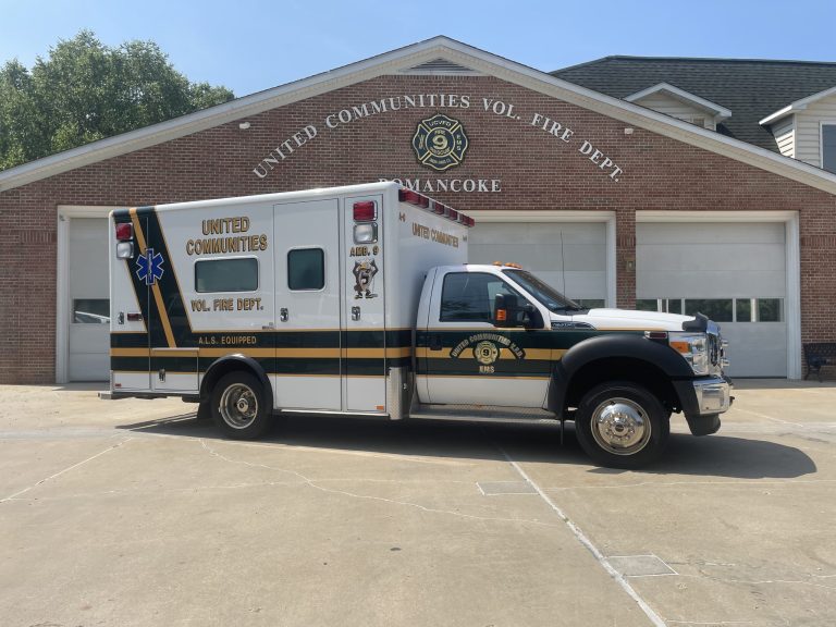 A white and green ambulance labeled "United Communities Vol. Fire Dept." is parked in front of a brick fire station with "United Communities Vol. Fire Dept. Romancoke" written above the garage doors.
