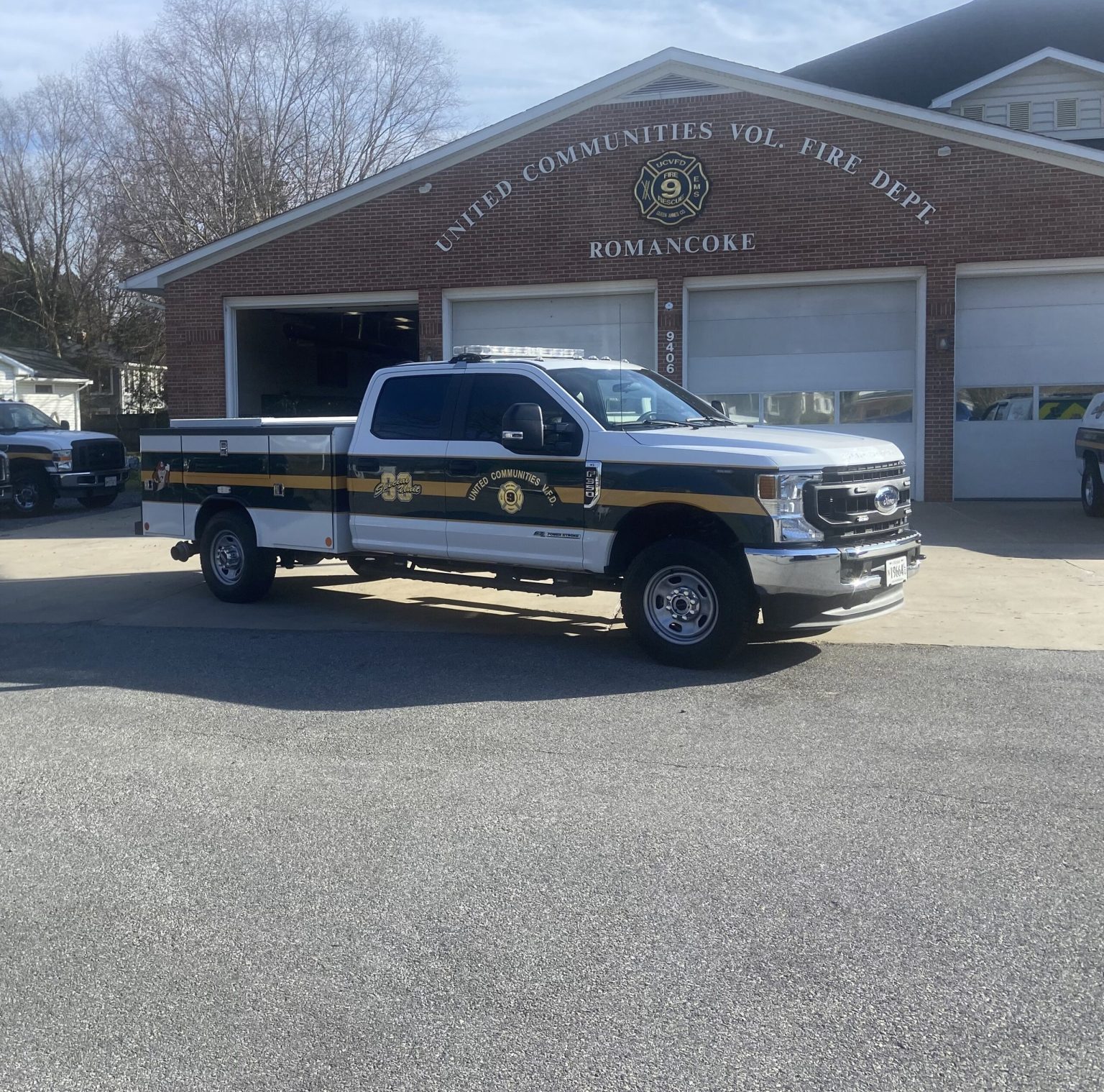 A white and black United Communities Volunteer Fire Department truck is parked in front of a brick fire station building labeled "ROMANCOKE" under a clear sky.